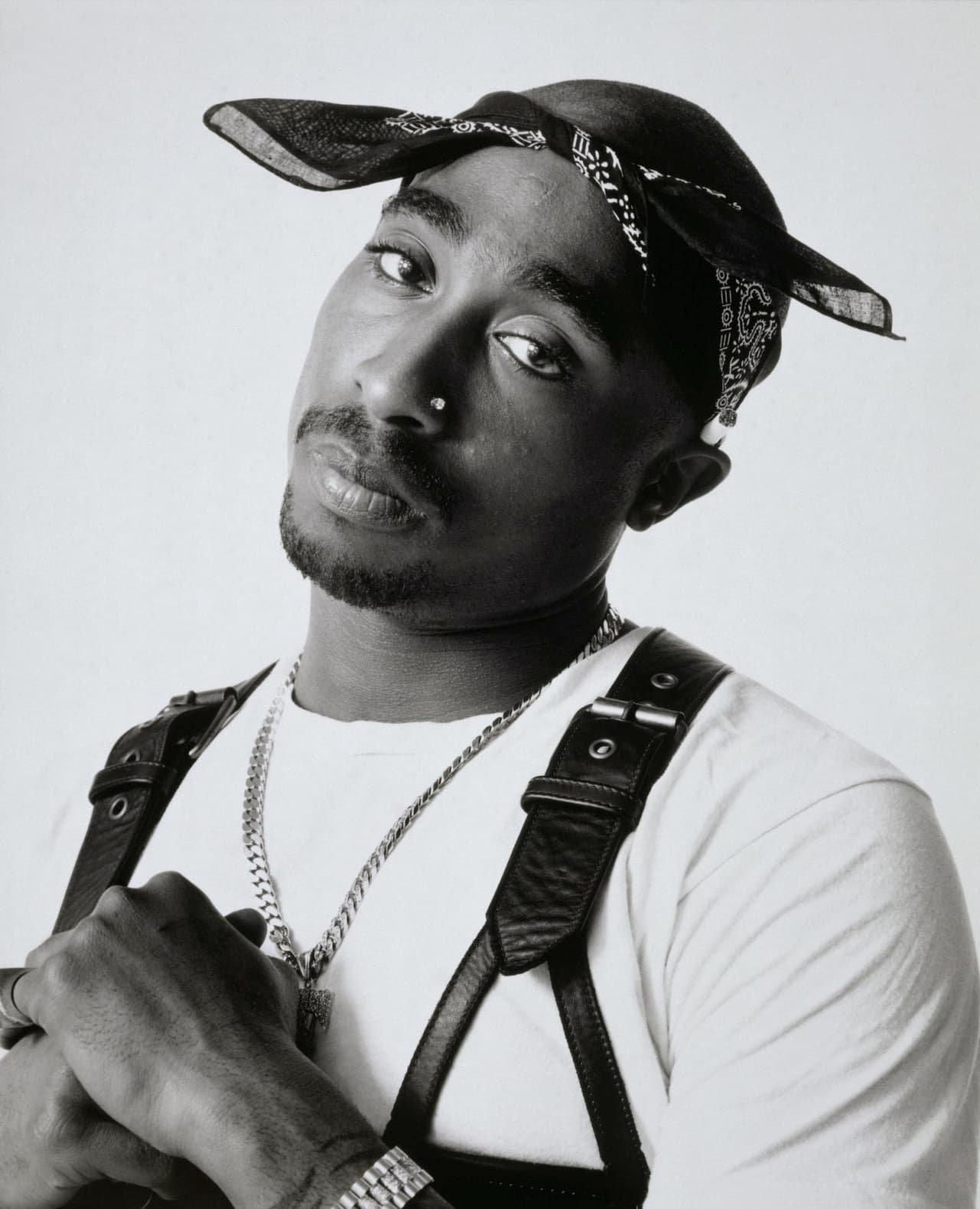Black and white portrait of Tupac Shakur wearing a bandana, nose stud, and leather harness.